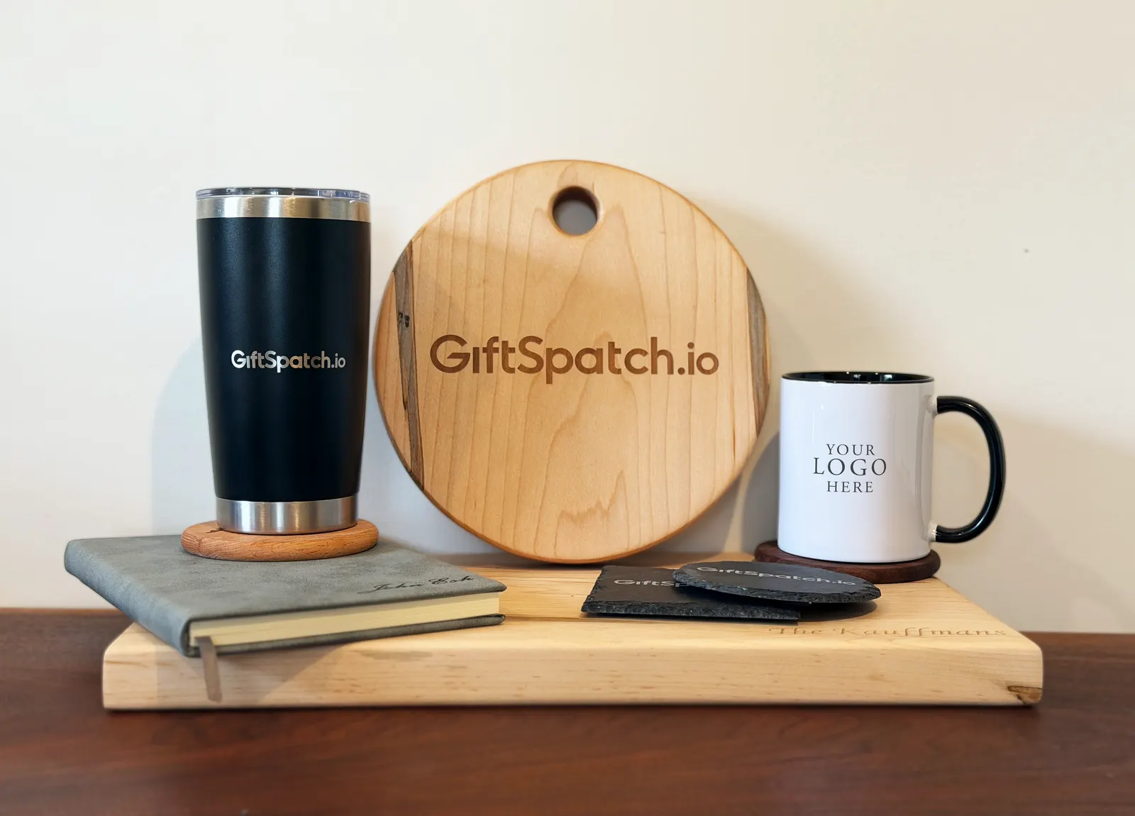 A branded tumbler, round maple board, journal and mug on a wooden shelf